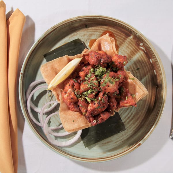 Top-down view of a dish with red chicken pieces, cilantro, lemon, and onion on a plate.