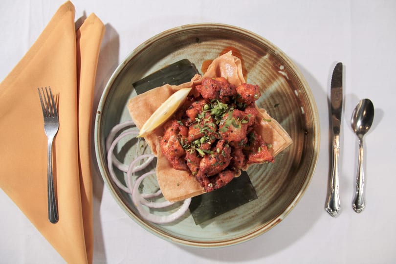 Top-down view of a dish with red chicken pieces, cilantro, lemon, and onion on a plate.